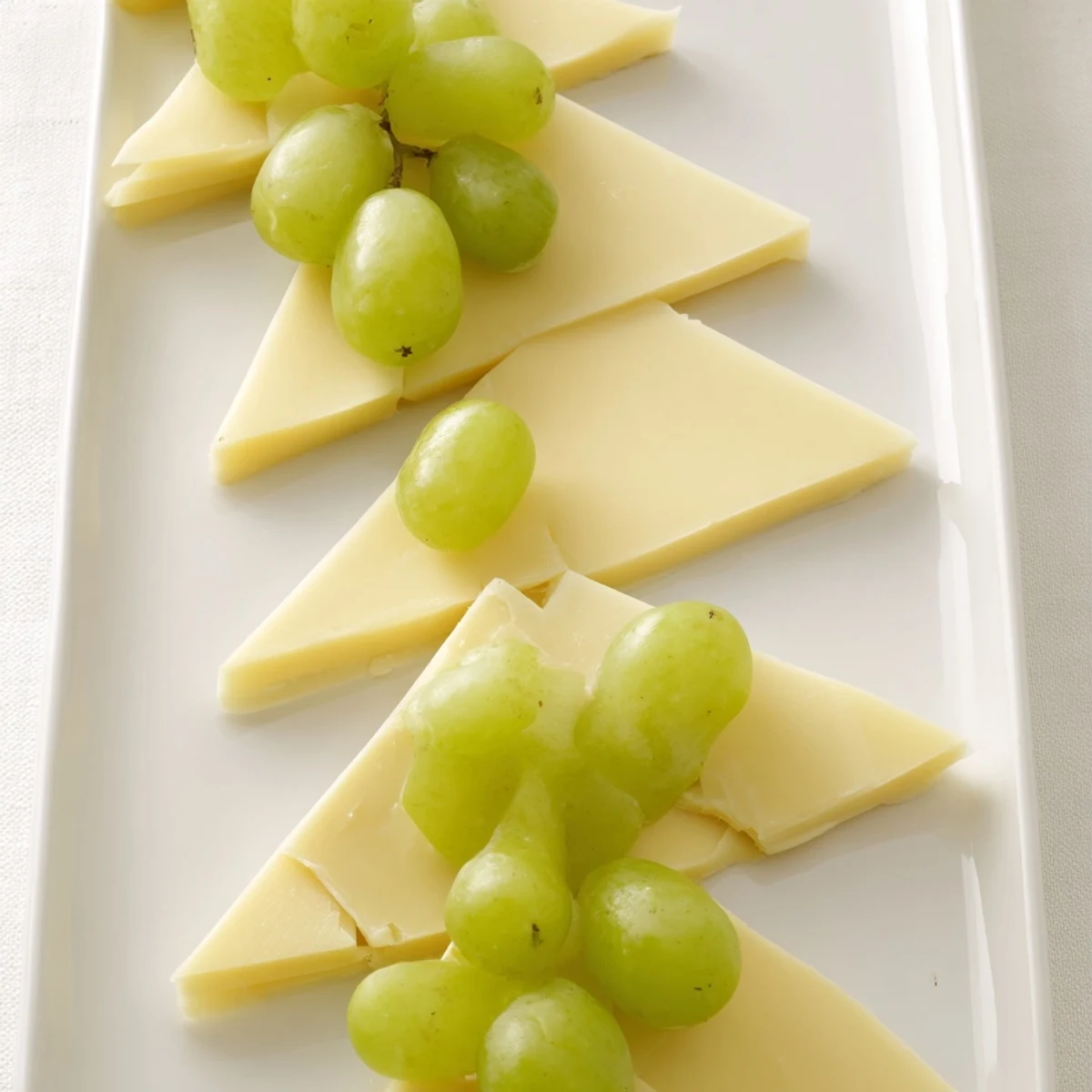 A visually stunning, festive The Tannenbaum Border cheese board featuring triangular cheese "trees" and grapes.