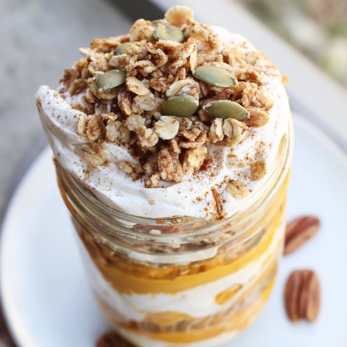 A layered Pumpkin Yogurt Parfait, bright orange pumpkin against creamy white yogurt, topped with crunchy granola.