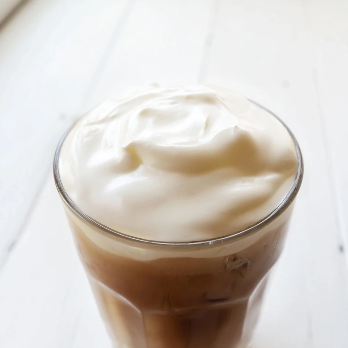 Fluffy Starbucks Cold Foam: creamy white topping swirling atop a dark iced coffee, perfect for summer.