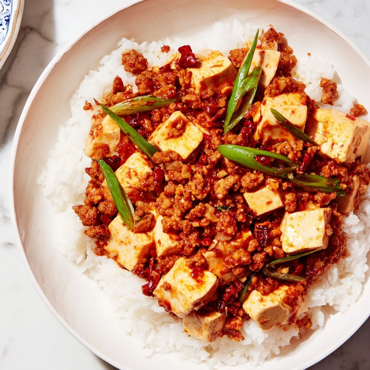 Steaming hot Chinese Mapo Tofu with vibrant scallions atop fluffy rice, ready to eat.