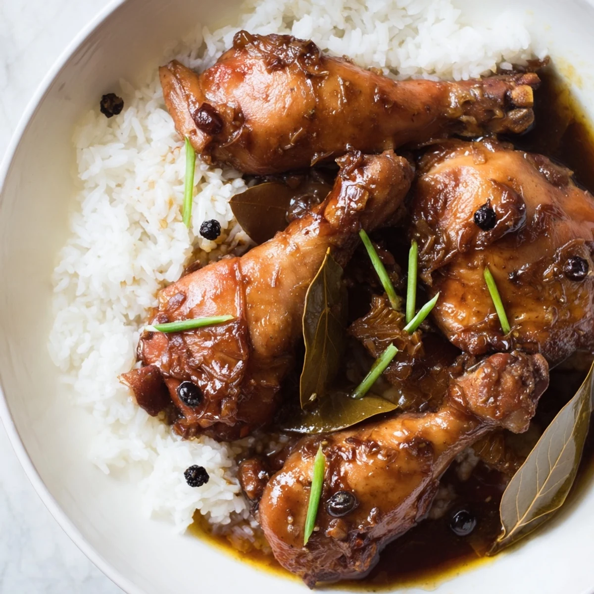 Tender Filipino Chicken Adobo served over fluffy white rice, glistening with rich, savory sauce.
