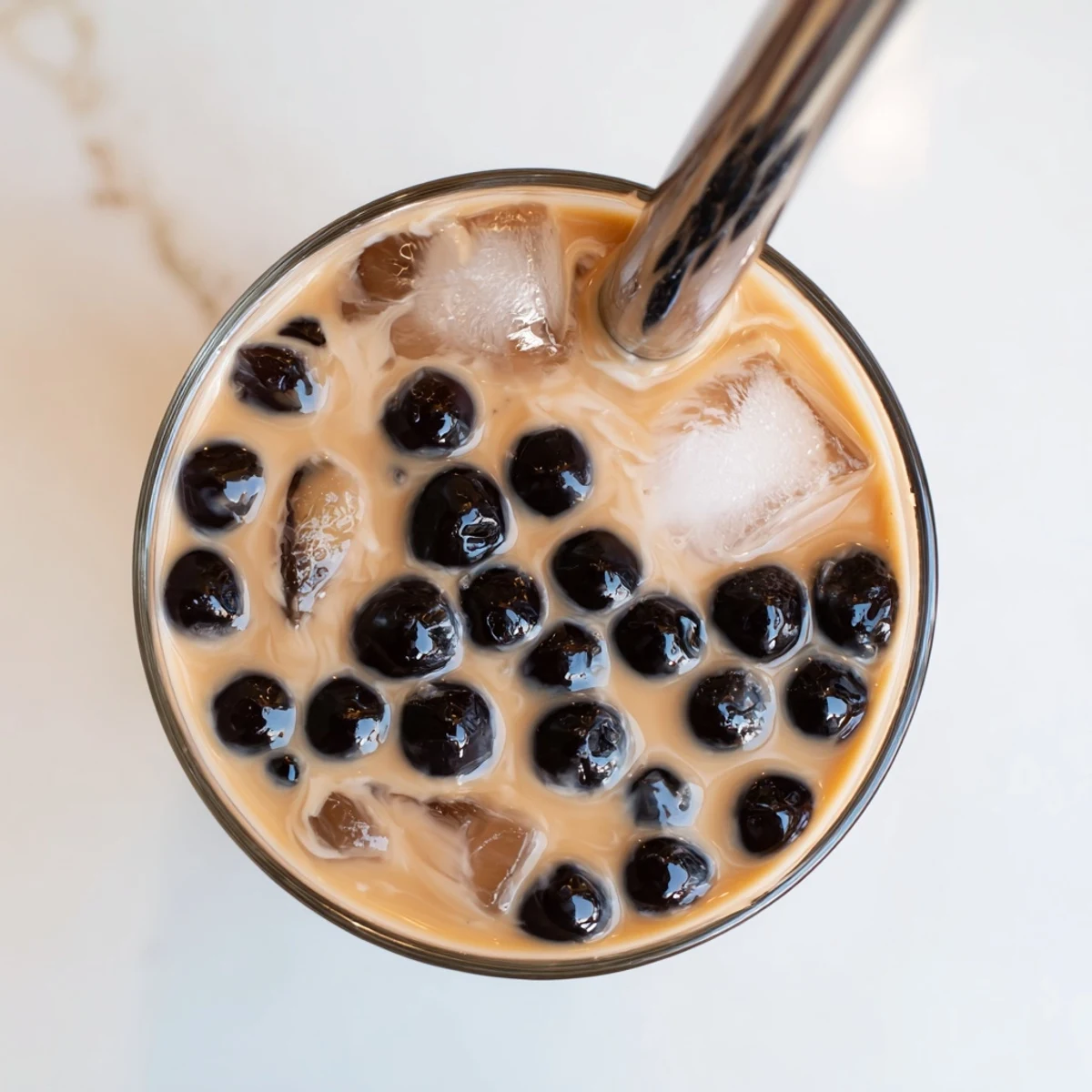 Glossy boba pearls rest in creamy Boba Tea Hack – Instant Bubble Tea with Sweetened Condensed Milk, served over ice with a striped straw.
