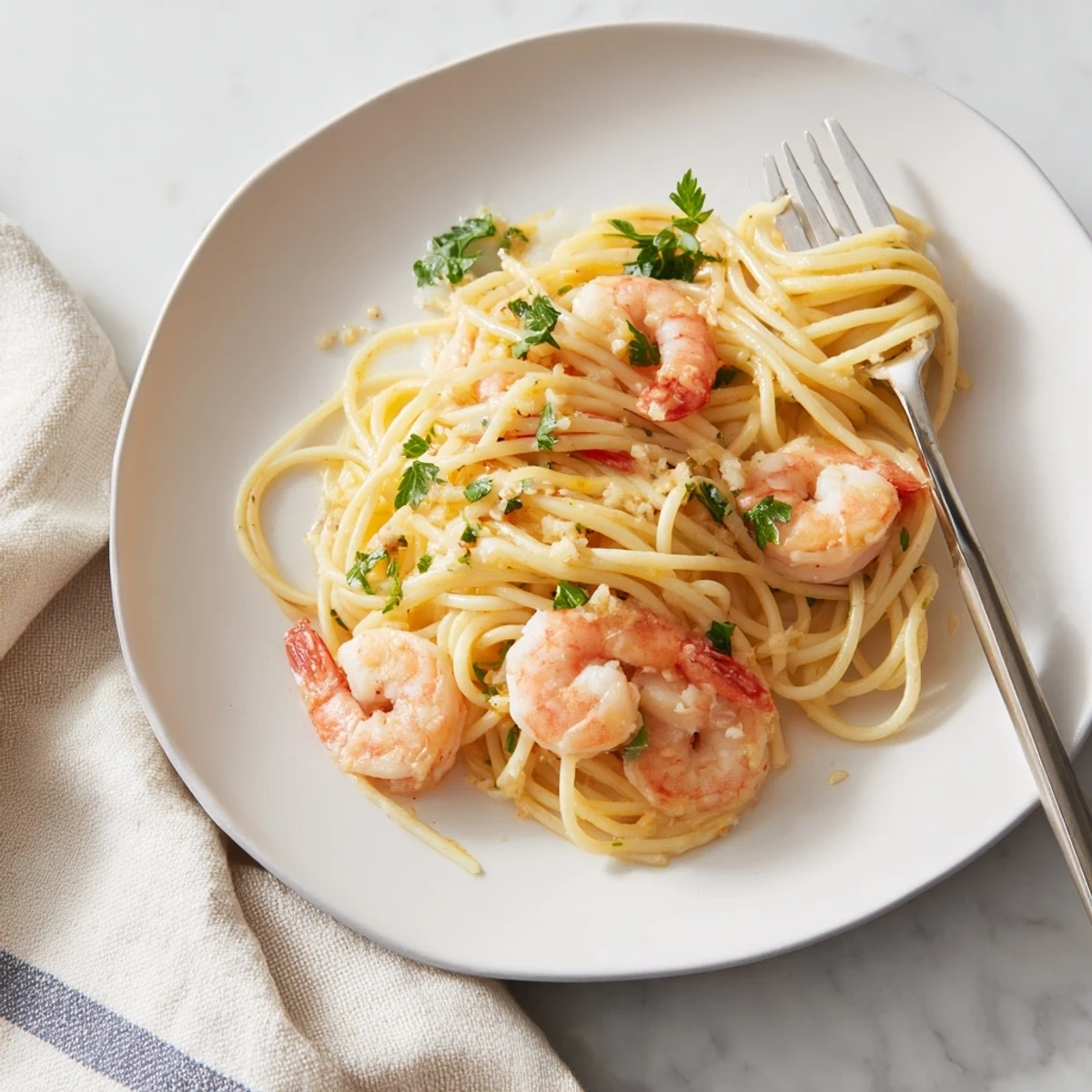 Golden spaghetti strands glisten with lemon garlic butter sauce, topped with plump pink shrimp and fresh parsley garnish.