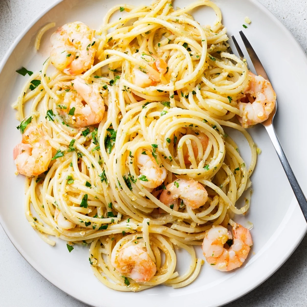 A close-up shows tender sautéed shrimp tangled in al dente pasta with zesty lemon and aromatic garlic.