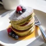 Stacked Egg White Gingerbread Matcha Soufflé Pancakes, dusted with powdered sugar, offering a delightful aroma and texture.