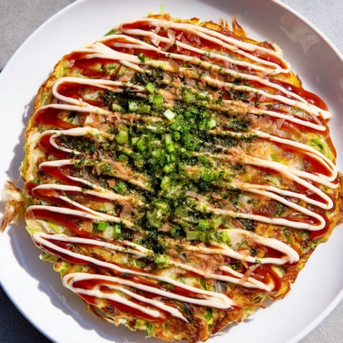 Golden, crispy Japanese Okonomiyaki pancake topped with savory okonomiyaki sauce and dancing bonito flakes.