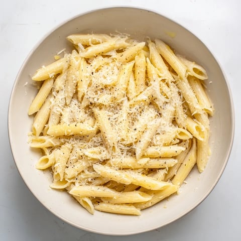 A close-up of microwave bowl pasta with penne coated in marinara sauce, garnished with Parmesan and black pepper for a quick, easy dinner.