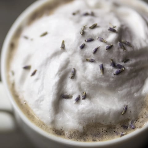 Creamy Whipped Lavender Latte served in a rustic ceramic mug on a wooden table.