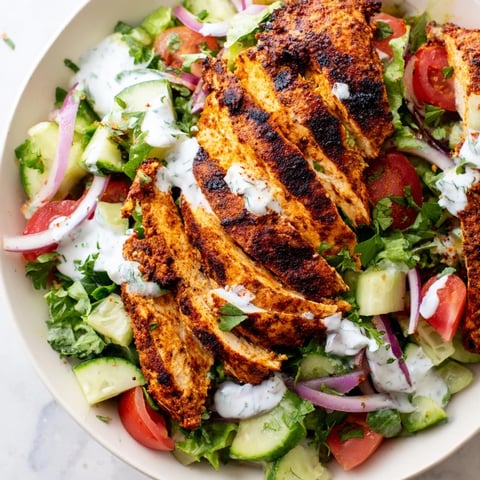 Sliced, spiced grilled chicken rests atop a crisp salad with cucumber, tomato, and parsley, drizzled with creamy Greek yogurt dressing.  