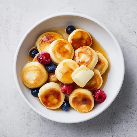 Fluffy mini pancakes, known as Pancake Cereal, topped with fresh berries, perfect for breakfast.