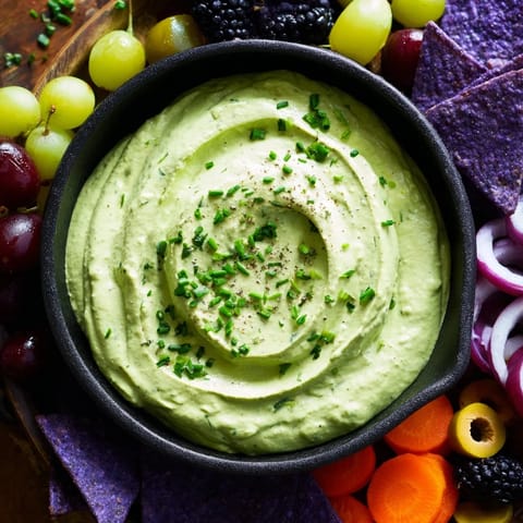 Vibrant green Witch's Brew Cauldron dip with dark fruits, chips, and a smoky red onion border.