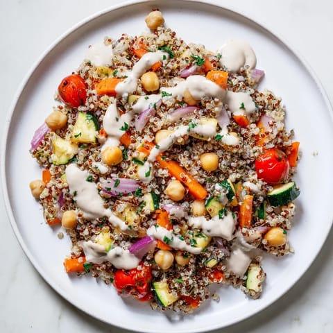 This quinoa power salad showcases colorful roasted vegetables and a zesty lemon-tahini dressing drizzled over it.