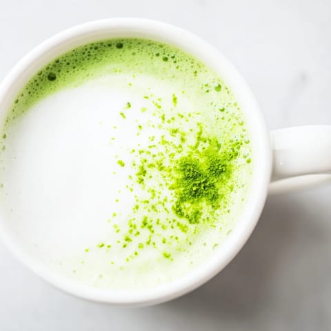 A freshly whisked matcha latte with creamy steamed milk and a golden drizzle of honey on a cozy morning table.  