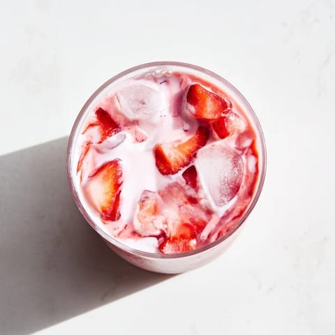 A close-up of the creamy Refresher Copycat Pink Drink, with ice cubes glistening beside sliced strawberries.