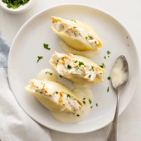 A close-up of Chicken Alfredo Stuffed Shells on a plate, garnished with fresh parsley and garlic bread.