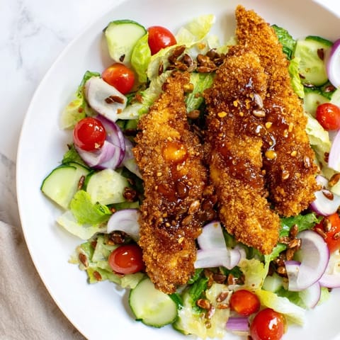 A close-up of Crispy Hot Honey Chicken Salad shows juicy breaded chicken on greens with cucumber, tomatoes, and a generous hot honey drizzle.