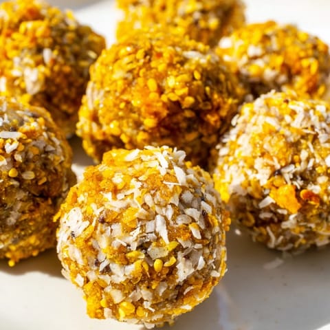 Close-up of vibrant orange-hued Ginger Turmeric Energy Balls with visible oats and hemp seeds, ready to enjoy after chilling.