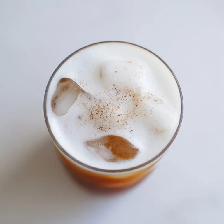 A tall glass filled with ice, amber-colored chai concentrate, and a thick layer of cold foam, perfect for a warm afternoon.