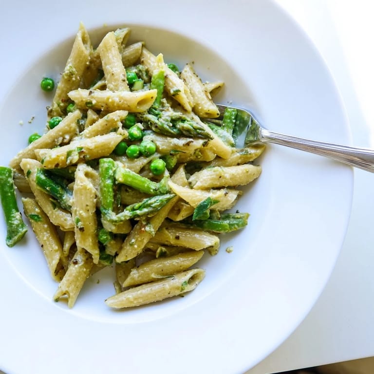 Overhead view of a large skillet filled with Garlic Parmesan Spring Vegetable Pasta, garnished with fresh basil and a lemon wedge for a bright, fresh finish.