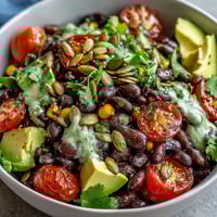 A close-up of a Black Bean and Veggie Bowl with creamy avocado, juicy tomatoes, and fresh cilantro on a rustic table.