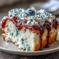 Memorial Day Red White Blue Poke Cake with vibrant gelatin swirls and whipped topping, decorated with patriotic sprinkles and fresh berries.  